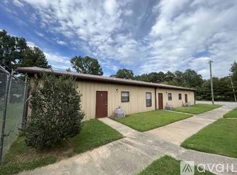 A building with a brown door and windows is surrounded by a grassy area and a fence.