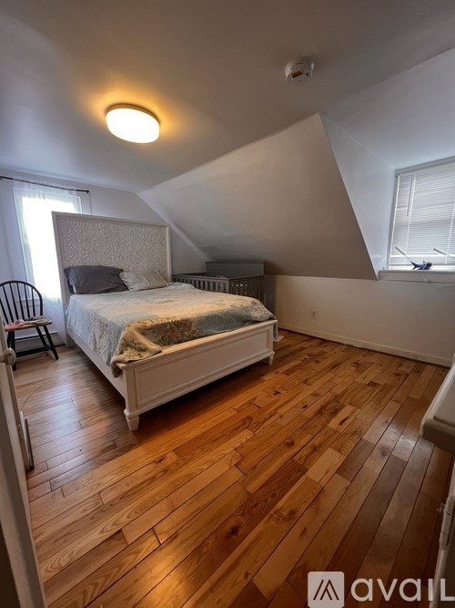 A bedroom with a bed, chair, and wooden floors.