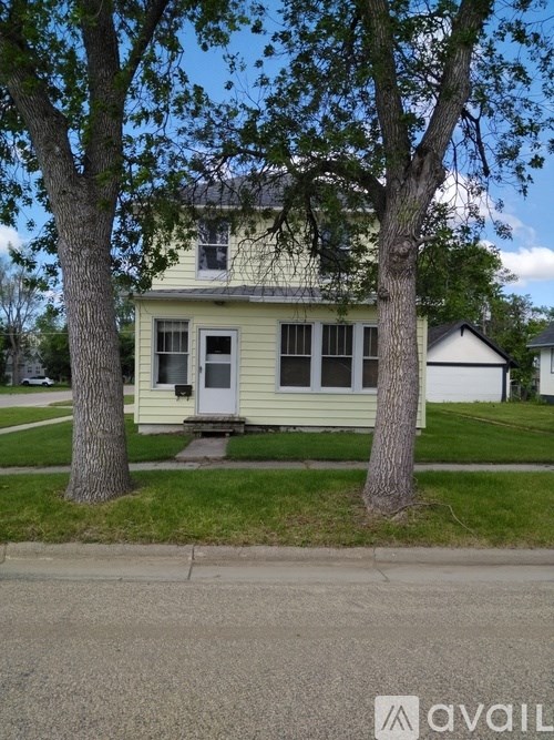 A house with a white door and windows is surrounded by trees.
