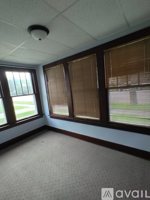 A room with a carpeted floor, a window with blinds, and a ceiling light.