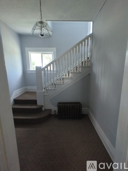 A carpeted staircase with a metal railing and a light hanging from the ceiling.