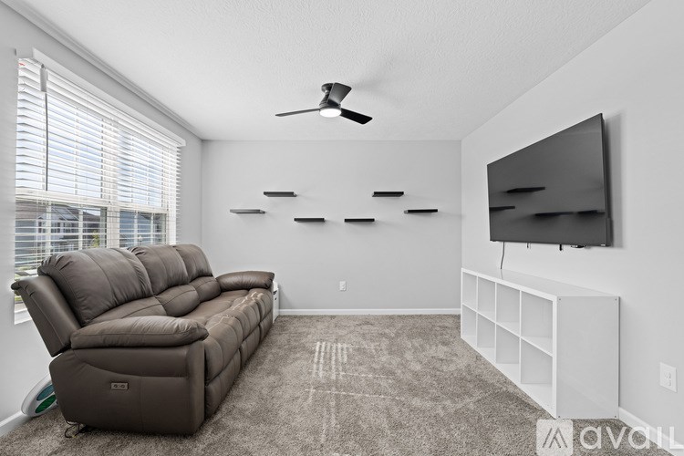 A living room with a brown sofa and a flat screen TV mounted on the wall.