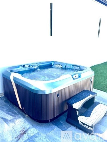 A hot tub with a seat and a footrest is on a patio.