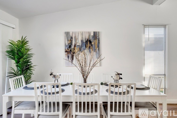A white dining table set with plates and cutlery is surrounded by white chairs.