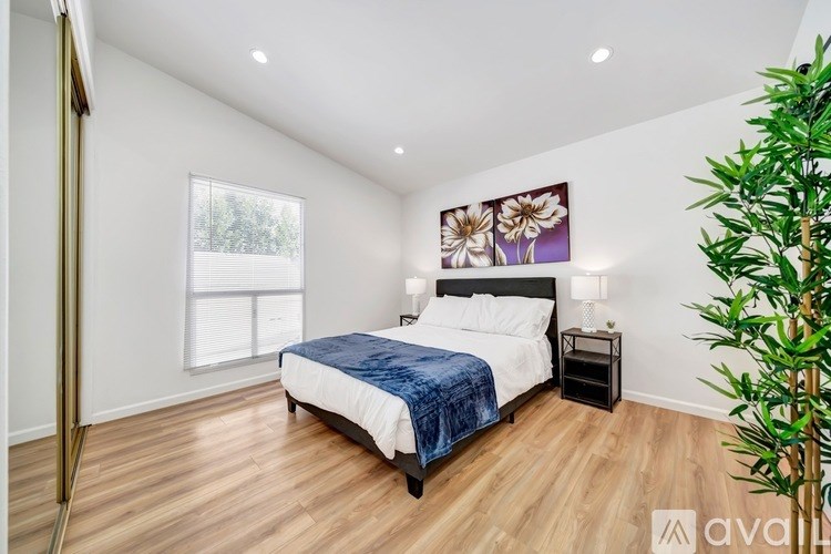 A bedroom with a bed, nightstand, and a plant.