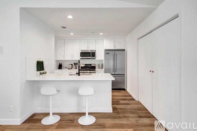 A kitchen with white cabinets and a white island with two stools.
