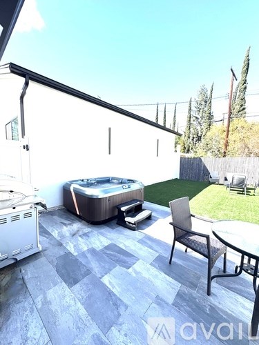 A hot tub sits on a patio with a chair and table.