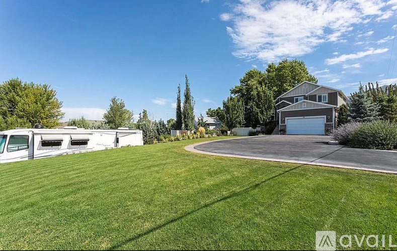 A house with a garage is situated in a green field with trees.