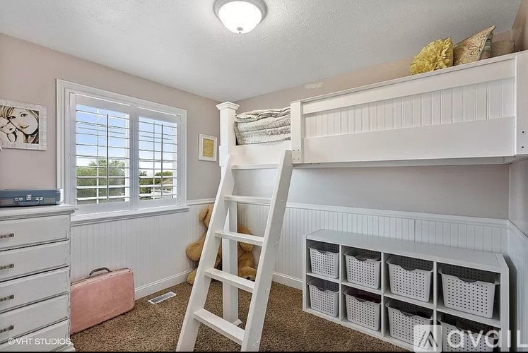 A room with a ladder, bunk beds, and a window with blinds.