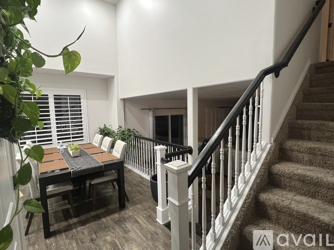 A dining table with chairs and a potted plant sits in a room with a staircase.