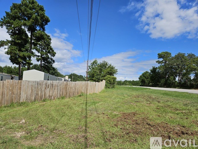 A grassy field with a wooden fence and trees in the distance under a blue sky.