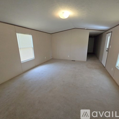 A spacious room with a carpeted floor and a window with blinds.