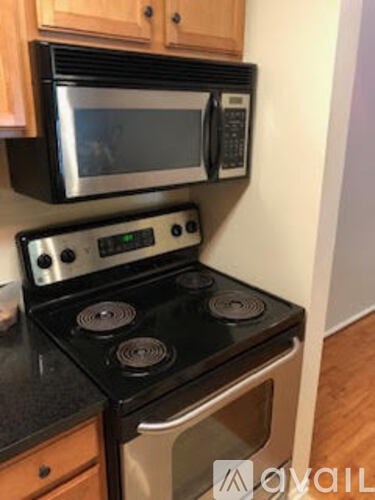 A black stove top oven with a digital clock and a silver microwave above it.