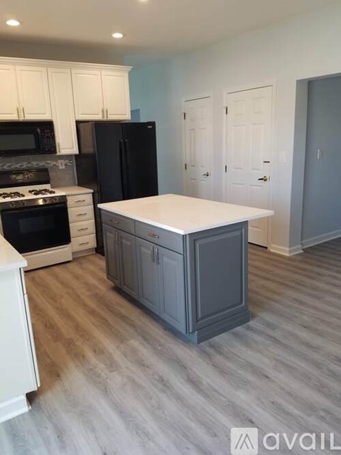 A kitchen with a black refrigerator, white cabinets, and a white island.