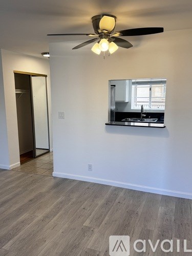 A room with a ceiling fan and a window overlooking a kitchen.