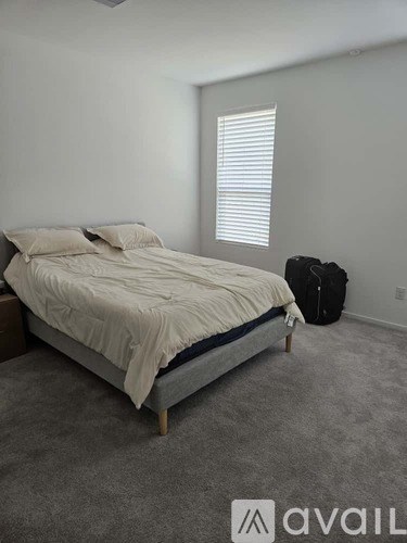 A bedroom with a bed, a suitcase, and a window with blinds.