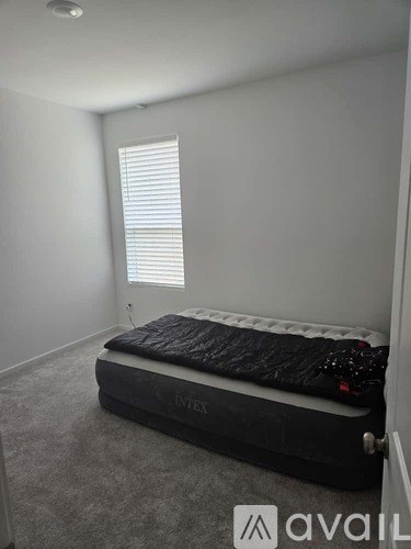 A bed with a black mattress and a white pillow is in a room with a window.