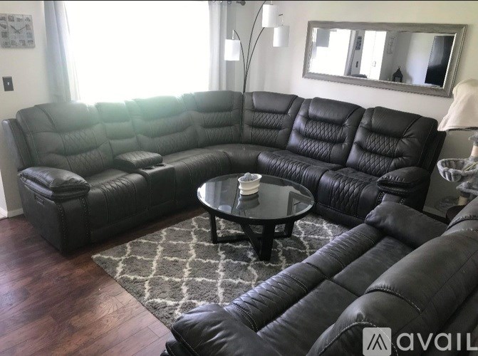 A black leather sectional sofa with a round glass table in the middle.