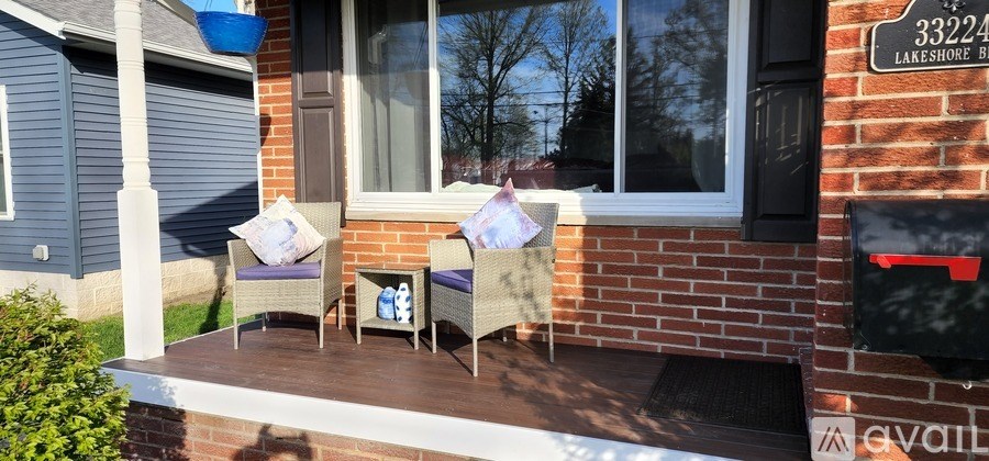 Two chairs are on a porch with a mailbox on the wall.