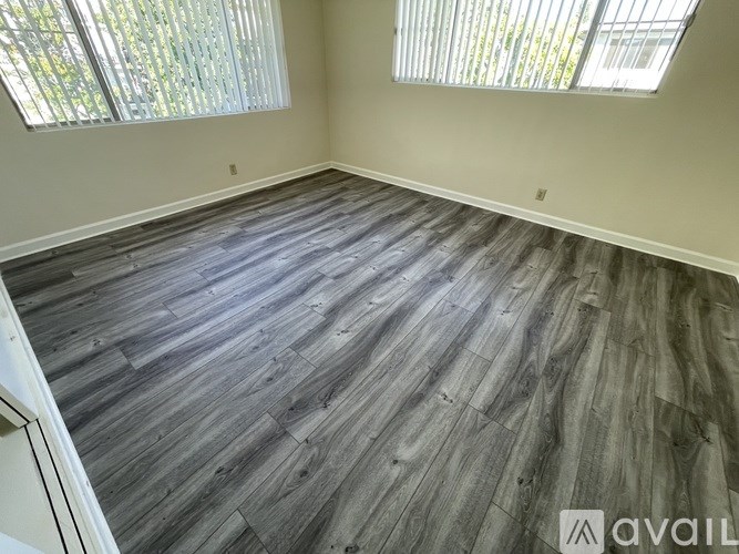 A room with wooden flooring and two windows.