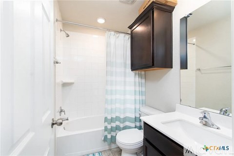 A bathroom with a white toilet, a white sink, a white bathtub, a white shower curtain, a white door, a white wall, a brown cabinet, and a white floor.
