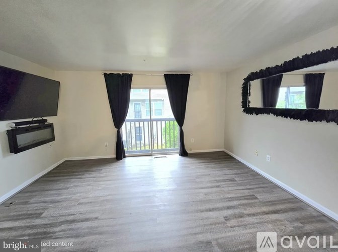 A spacious living room with a flat-screen TV and a sliding glass door leading to a balcony.