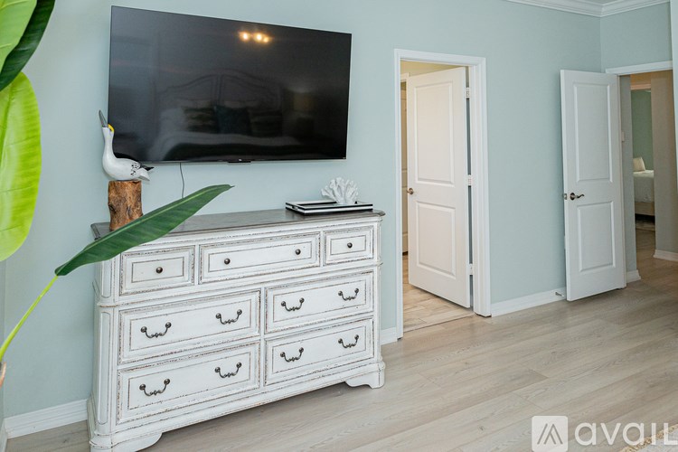 A white dresser with a flat screen TV mounted above it in a room with light blue walls.