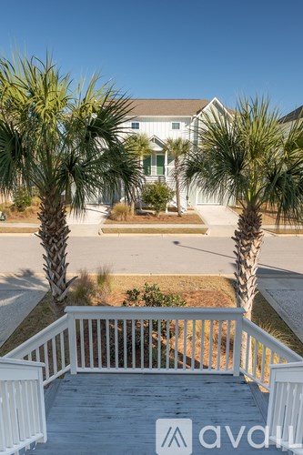 A white house with a porch and palm trees in front.