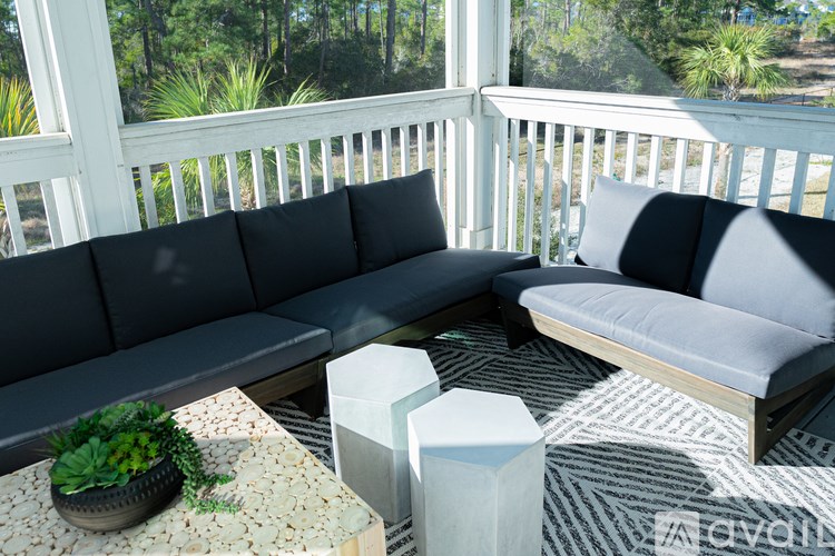 A black couch sits on a patio with a potted plant on a table in front of it.