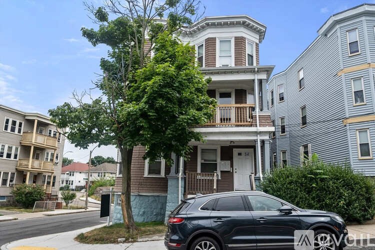 A black SUV is parked in front of a two-story house with a white door and a balcony.