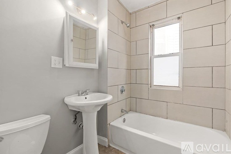 A white sink sits under a mirror in a bathroom with a white tub and a window.