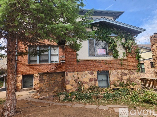 A house with a red brick facade and a stone wall is surrounded by greenery.