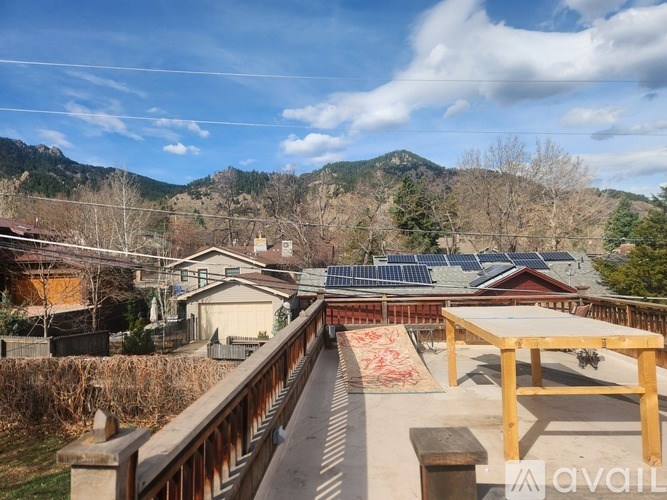 A wooden deck with a table and chairs overlooks a residential area with houses and trees.