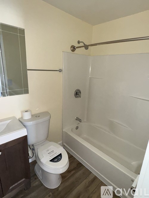 A white toilet with a roll of toilet paper on top sits next to a white bathtub in a bathroom.