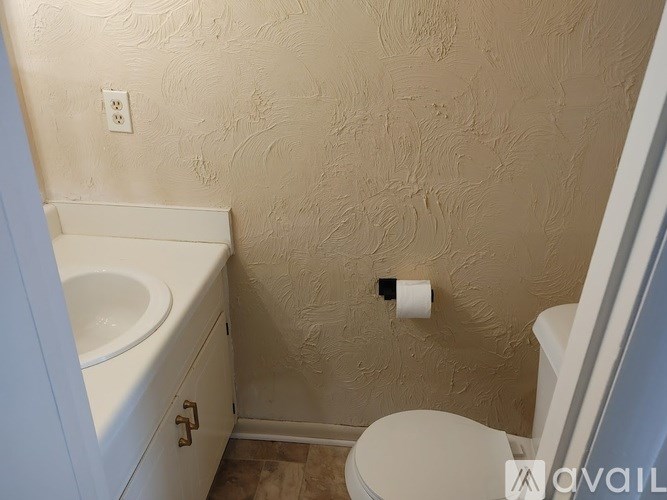 A bathroom with a toilet, sink, and textured wallpaper.