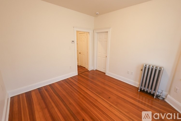A room with wooden floors and a white wall with a door and a radiator.