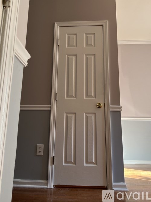 A white door with a gold handle is in a room with a grey wall.