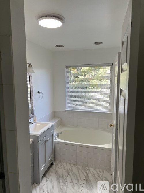 A bathroom with a white tub, sink, and tiled floor.