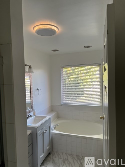 A bathroom with a white tub, sink, and window.