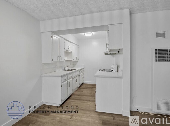 A white kitchen with wooden floors and a logo for Beach Front Property Management.