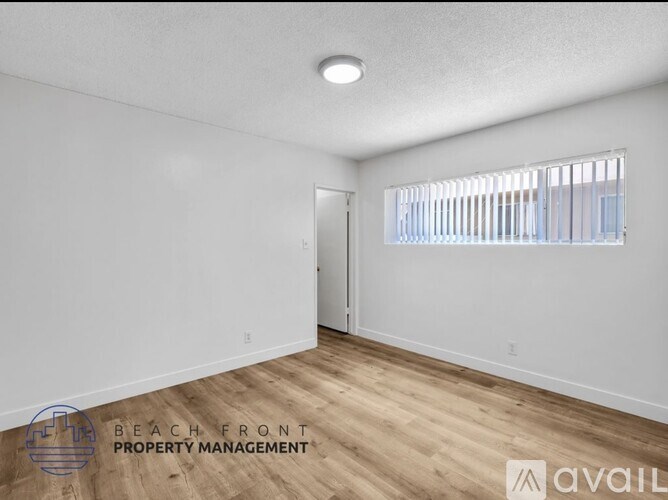 A spacious room with wooden flooring and a window with blinds.