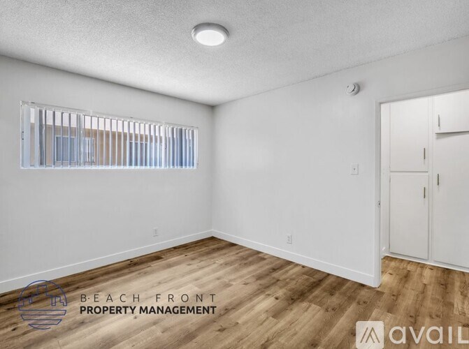 A room with wooden flooring and white walls, with a window covered by blinds, and a door on the right side.