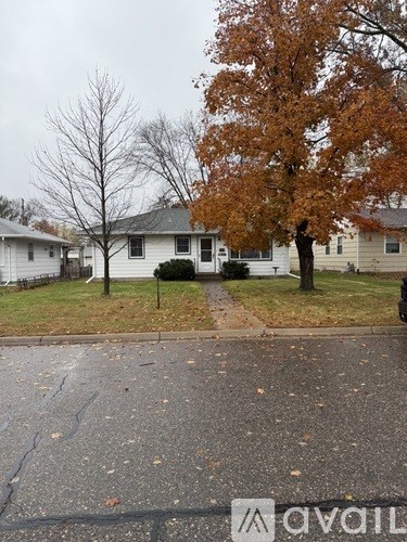 A tree with orange leaves stands in front of a white house.