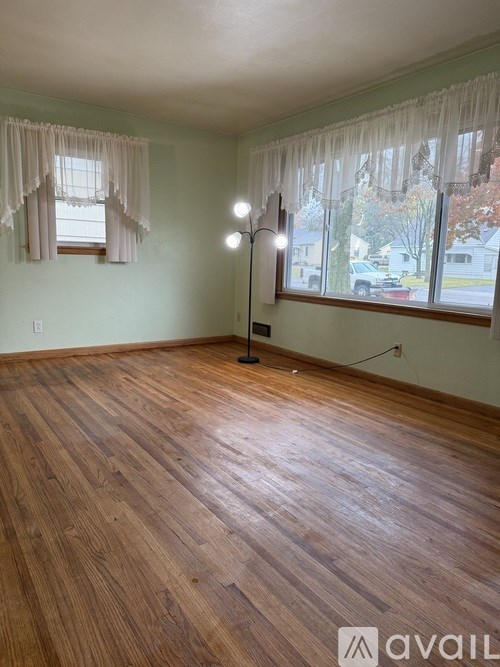 A room with wooden flooring and two windows with curtains.
