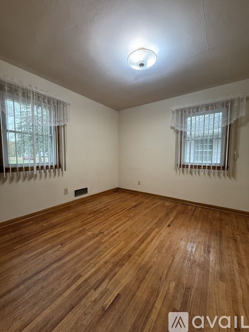 A room with wooden flooring and two windows with curtains.