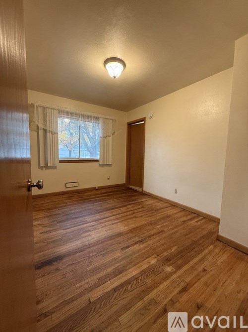 A room with wooden flooring and a window with white curtains.
