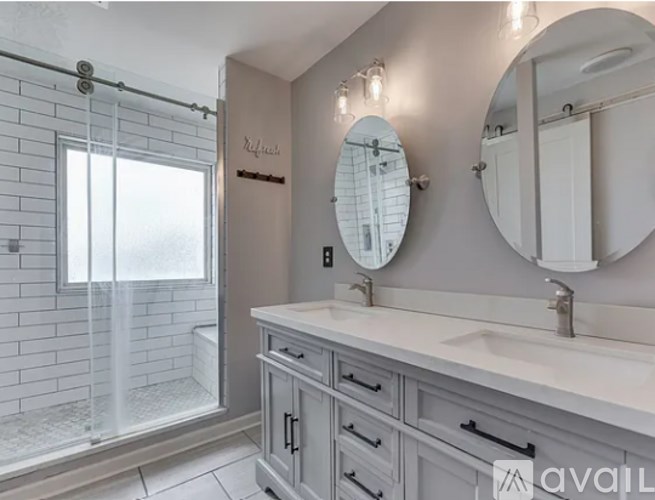 A bathroom with a white sink, a round mirror, and a shower with a glass door.