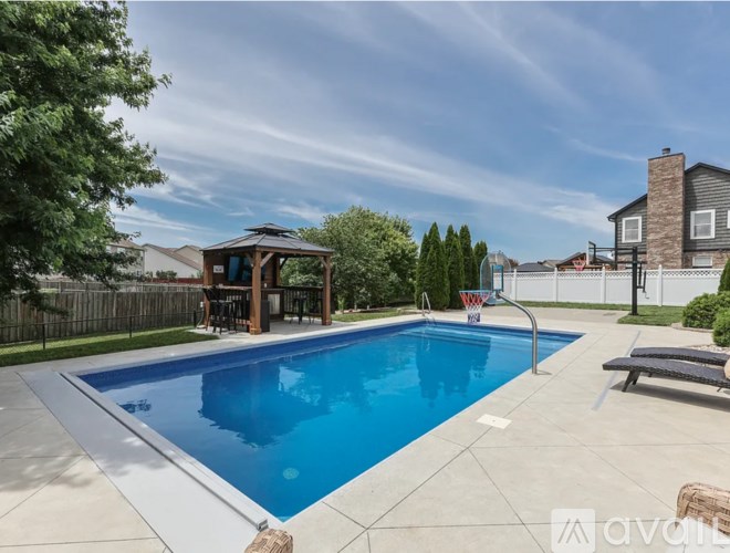 A swimming pool in a backyard with a pavilion and a basketball hoop.