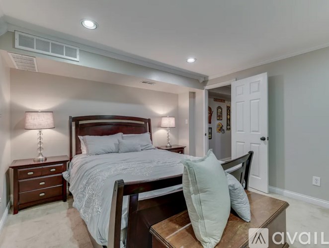 A bedroom with a large bed, a nightstand with a lamp, and a chair with a pillow on it.