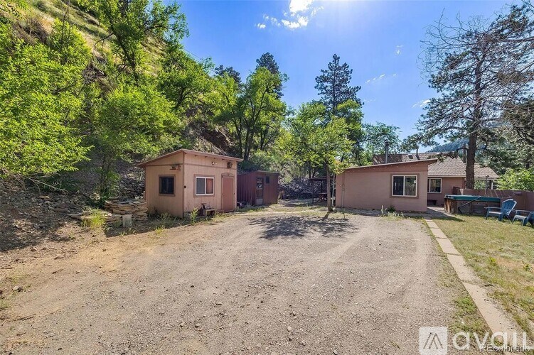 A house with a brown roof is surrounded by green trees and a gravel driveway.